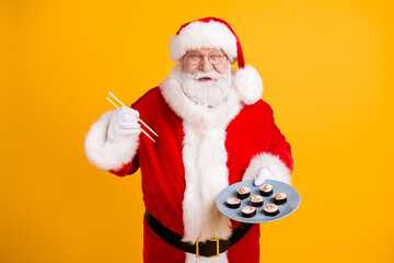 Portrait of his he nice cheerful cheery funny glad white-haired Santa enjoying eating fresh seafood tasty yummy sushi isolated bright vivid shine vibrant yellow color background