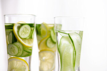 closeup of three glasses of cucumber and lemon refreshing drink decorated with sliced lemon and cucumber on marble table with white background.