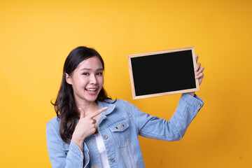 Fototapeta na wymiar A young Asian woman smiling with bright and excited faces, pointing fingers on the sign held on hand with an orange background. Asia woman, woman concept.