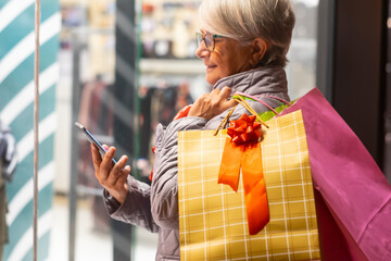 Senior woman enjoying evening shopping looking at her smart phone. Concept of consumerism and...