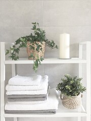 Stacked white and gray towels on a white shelf against a gray ceramic tile wall