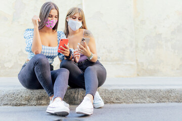 Naklejka premium serious women with a face mask looking at a smart phone, checking the news on a street curb