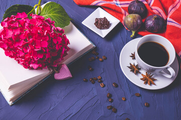 a cup of aromatic coffee, an open book and a branch of hydrangea on a blue background