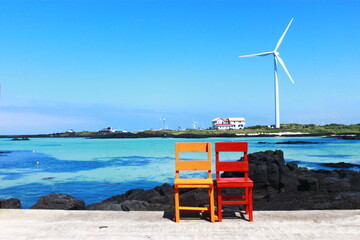 Blue sky, beach, ocean, wind turbines and a colorful chair in Jeju Island, Korea