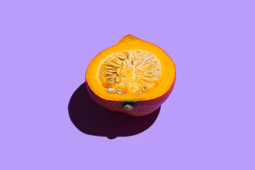 Halved orange pumpkin on neon purple background. Conceptual food minimal concept