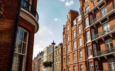Fototapeta premium Looking up at red brick London townhouses against blue sky