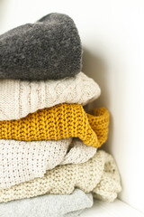 Cozy knitted sweater stack for cold autumn weather on white background. Stylish white, yellow and grey sweaters close up with space for text. Hello fall!