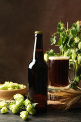 Beer, hop and wheat on wooden table against brown background