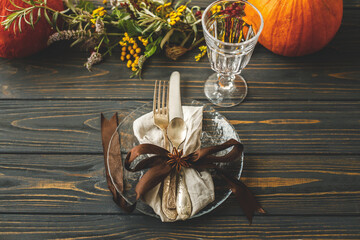 Thanksgiving dinner table setting. Stylish plate with cutlery and autumn decorations, pumpkin,...