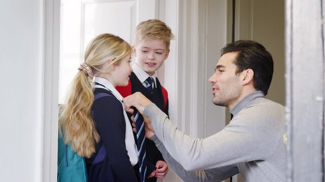 Father checking uniforms and straightening ties of son and daughter as they leave home for school - shot in slow motion