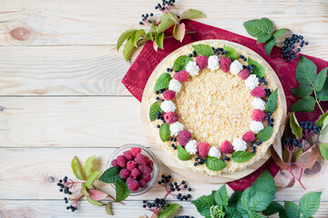 Napoleon cake with raspberries and cream on red napkin on light wooden background. Overhead view, copy space