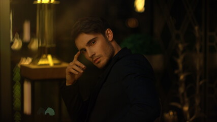 Pensive boss sitting in dark room. Young man touching face in blurred background