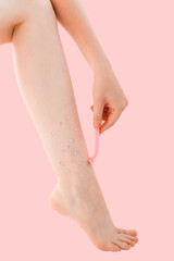 Woman's thin unshaven leg with sparkles on a pink background. Female shaves her leg with a pink razor. Feminism