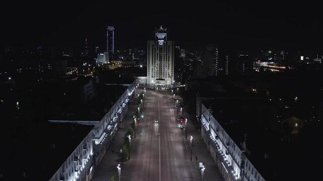 Aerial view of one of the central street in Ekaterinburg city at night. Stock footage. Flying along the houses decorated by shining lights towards the high rise building with unusual roof, concept of