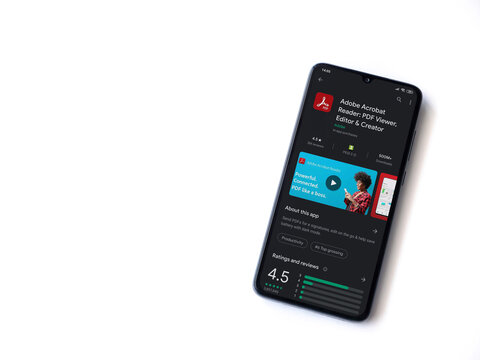 Lod, Israel - July 8, 2020: Adobe Acrobat Reader app play store page on the display of a black mobile smartphone isolated on white background. Top view flat lay with copy space.