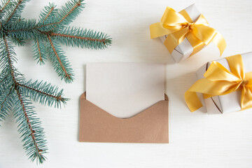 Christmas or New Years gifts with a gold ribbon and a fir branch on a light background. An envelope with a blank sheet of natural color. Postcard with space for your text.