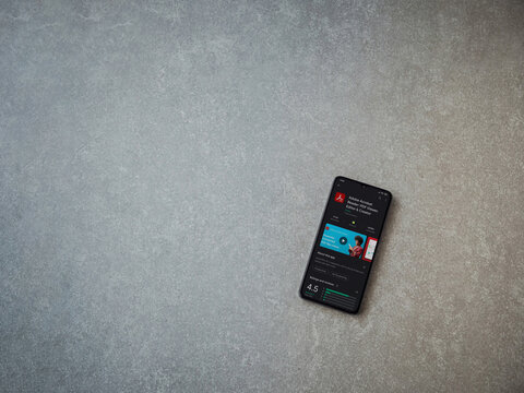 Lod, Israel - July 8, 2020: Adobe Acrobat Reader app play store page on the display of a black mobile smartphone on ceramic stone background. Top view flat lay with copy space.