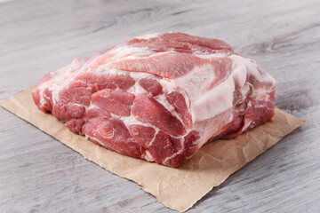 A piece of uncooked meat of pork neck on paper on gray table. Close up view.