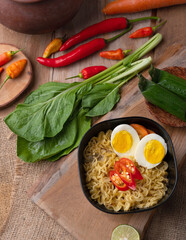 Fried noodles served on a wood cutting board with chilies, tomatoes, vegetables on the side