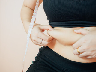 Lose belly fat concept from close up woman in sportswear with hand holding her own belly fat and...