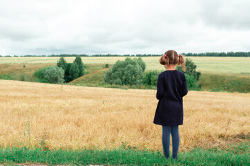 Child girl standing in a wheat field and looking into the distance. Copy space.
