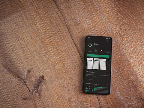 Lod, Israel - July 8, 2020: GitHub app play store page on the display of a black mobile smartphone on wooden background. Top view flat lay with copy space.
