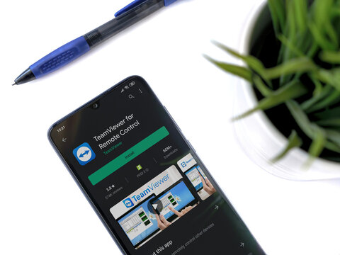 Lod, Israel - July 8, 2020: Modern minimalist office workspace with black mobile smartphone with TeamViewer app play store page on white background. Top view flat lay with copy space.