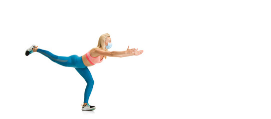 Beautiful female fitness coach practicing on white studio background, showing exercises. Caucasian model in sport outfit and face mask. Professional occupation, active and healthy lifestyle. Flyer