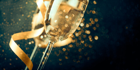 Two champagne glasses with golden ribbon and gold glitter splash bokeh on dark background. Luxury restaurant dinner celebration. Classy christmas and new year holiday panoramic design banner. © hitdelight