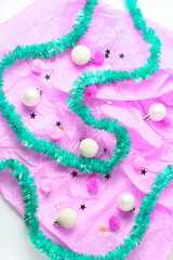 holiday concept. composition of brightly turquoise tinsel, balls, pomopons and confetti on a pink background. flat lay, top view.
