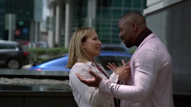 A African-Americanman and a white woman laugh and smile on the street in the background of a business center. Beautiful interracial couple are on a city street.
