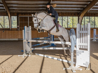 Start der Hallensaison im Reitsport: junge blonde Frau  auf Schimmel mit Knebeltrense beim Trainingsspringen in der Reithalle © mavcon