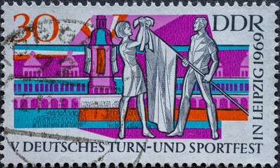 GERMANY, DDR - CIRCA 1969: a postage stamp from Germany, GDR showing male and female Truner with flag in front of the town hall in Leipzig. Text: German gymnastics and sports festival in Leipzig