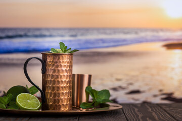 Cold Moscow Mules cocktail with ginger beer, vodka and lime over beach and seaside background