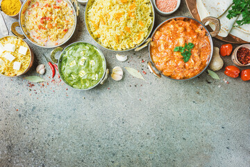 Different bowls with assorted indian food on gray stone background, top view. Dishes and appetizers of indian cuisine. Chicken, curry rice, lentils, paneer, chapati and spices.