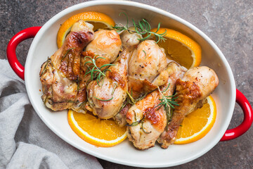 Baked chicken drumstick in a dish with orange and rosemary, top view