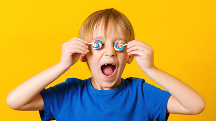 Child covered eyes with lolipops. Cute excited boy over yellow background.
