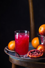 Glass of blood orange juice with ice and orange fruits on dark background