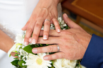 Obraz na płótnie Canvas groom man and bride woman closeup hands with wedding rings over marriage bouquet of natural flowers