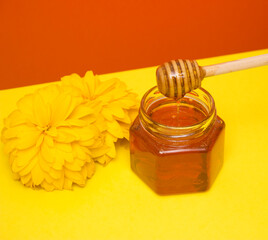 Bee honey drips from a wooden spatula into a glass jar. Flower, yellow-red background. Useful farm products.