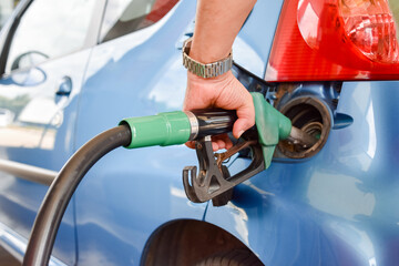 Male hand filling the tank of a car with fuel on a service gas station during a road travel