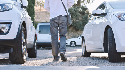 Detail of the legs of a commuter passing through an outdoor parking lot full of white cars