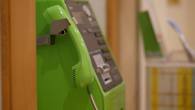 Woman hang up payphone and put handset on hook, close up shot with selective focus. Someone finish conversation using public phone, common green payphone used at Japan