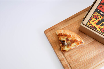 A slice of pizza on a wooden chopping board on white background