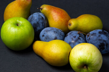Fruit on a black background. Plums, pears and apples lie side by side. Healthy fruits