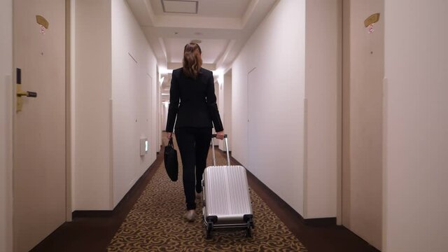 Business woman with small trolley case and laptop bag walk at corridor, super slow motion shot. Moving camera follow behind. Lady leave or arrive, go with confidence at long passage