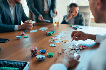 Playing poker, gambling on workplace. Happy carefree colleagues having fun in office while their co-workers working hard and highly concentrated. Concept of fun, resting, professional occupation.