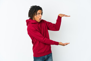 Young african american rasta man shocked and amazed holding a copy space between hands.