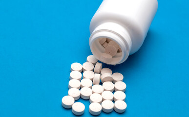 White pills scattered from a white bottle, jar on a blue background. Health care and treatment...