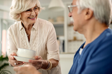 Obraz premium Happy senior woman bringing coffee to he husband at home.
